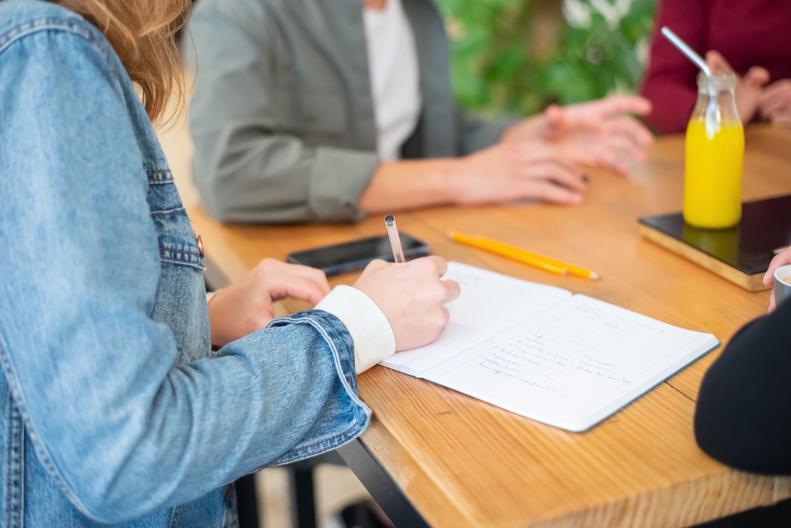 People sit around a wooden table, one writing in a notebook.