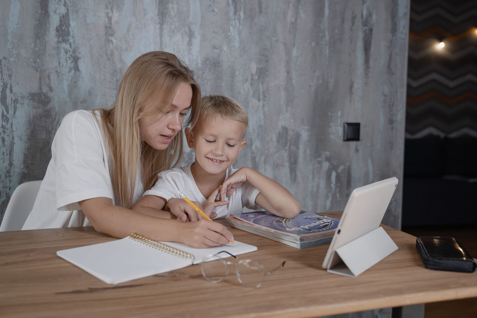 A woman helping a boy with his notebook at a kitchen table