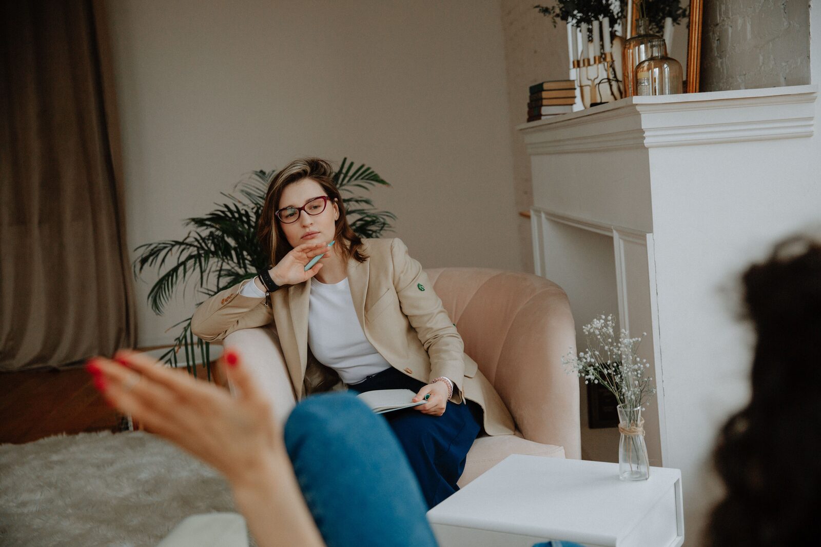 Two people talking in a sitting room. One listens, a notebook open on her lap.