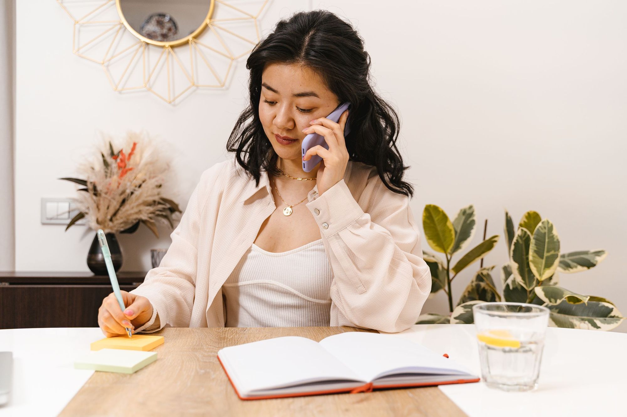 A woman on the phone taking notes at a bright table