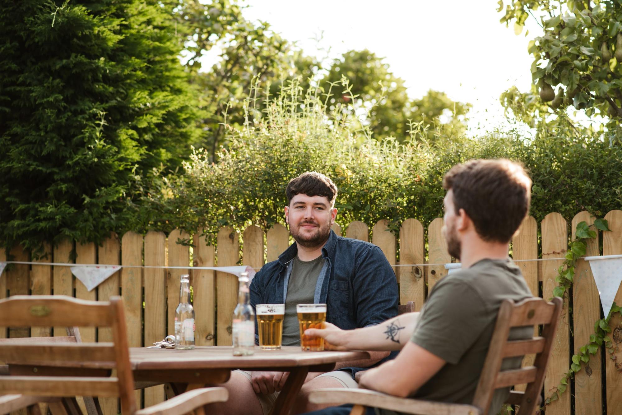 Two men talking at a table in a backyard