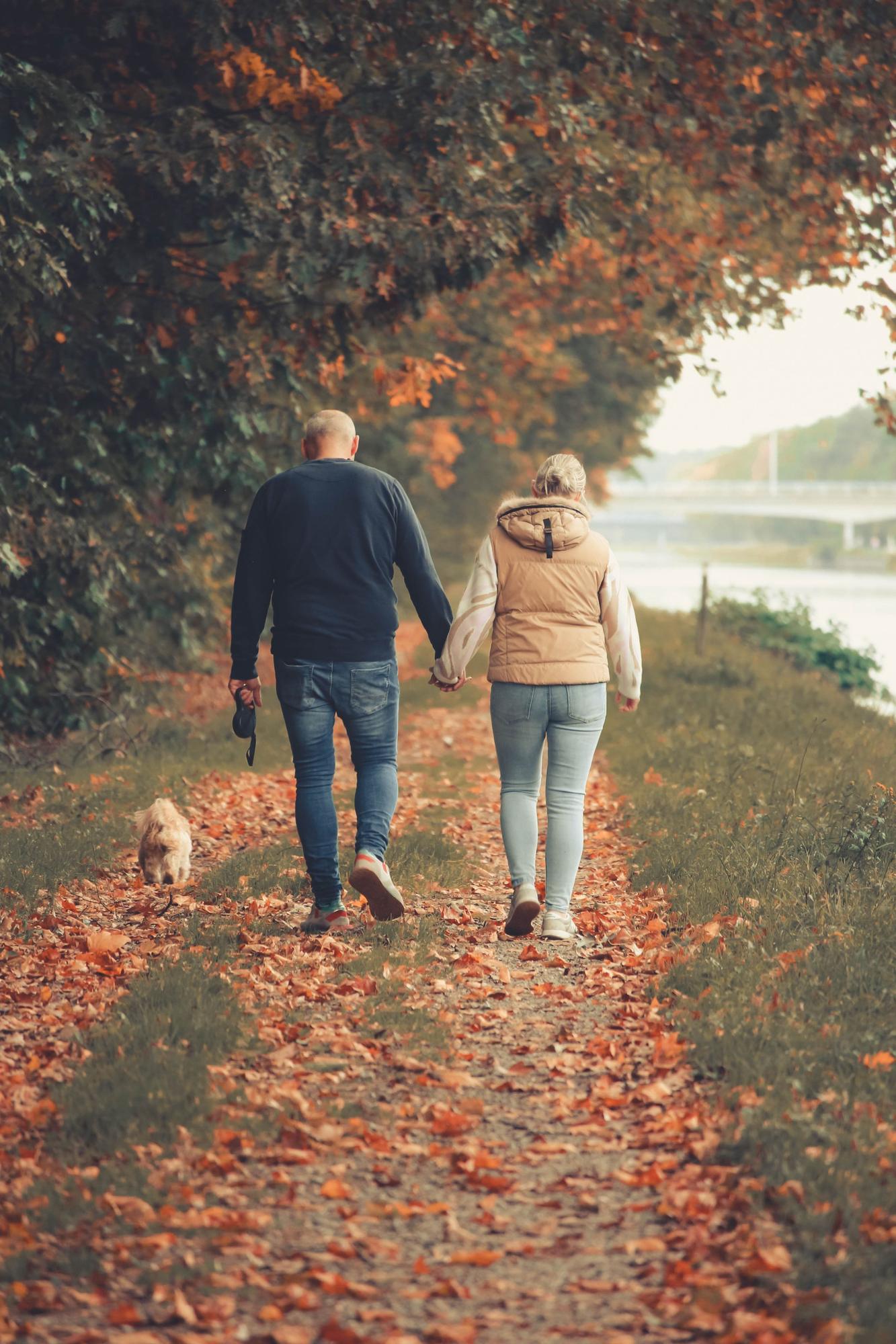 A couple walking hand in hand along a leaf-covered path