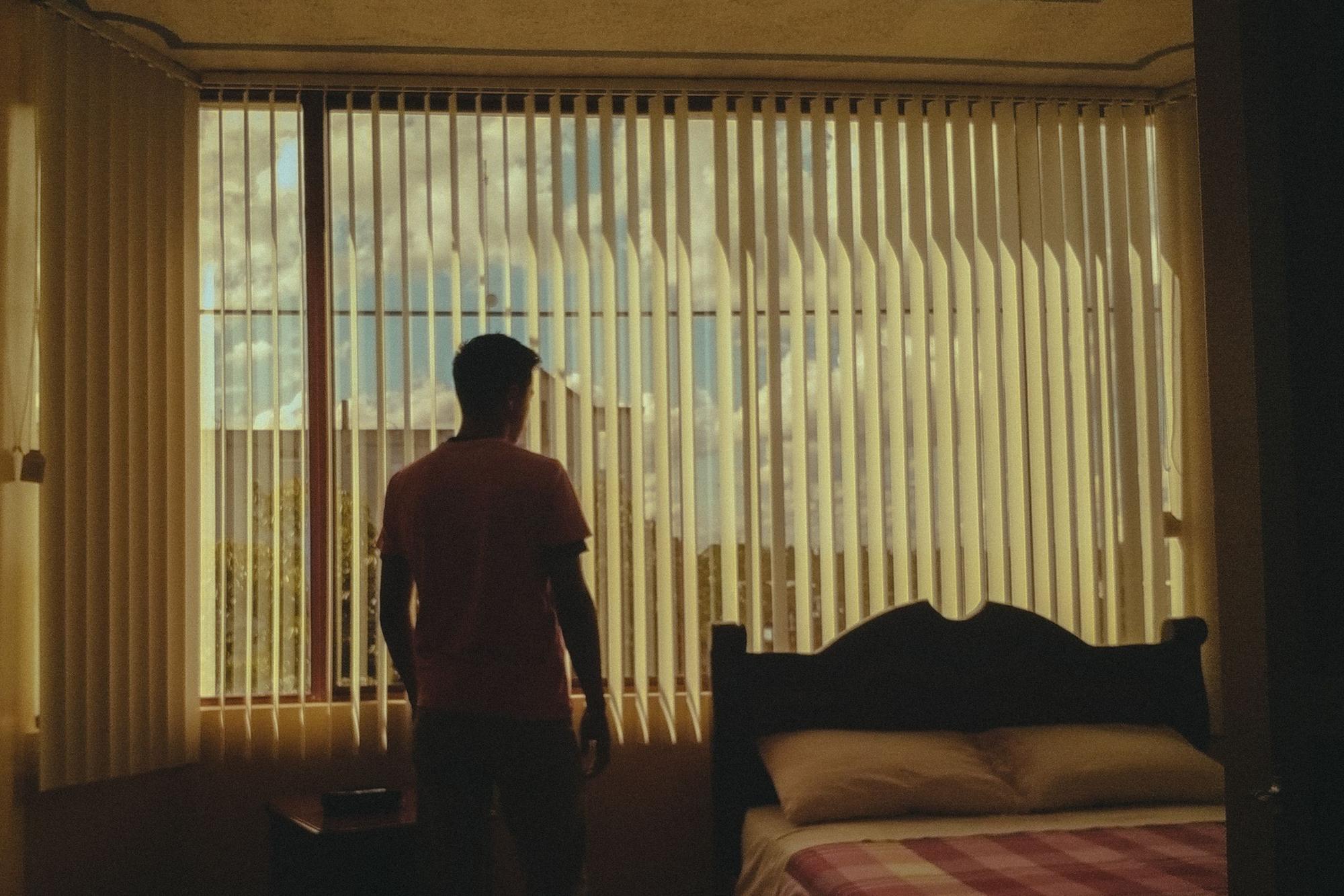 A man standing at a bedroom window in the morning light