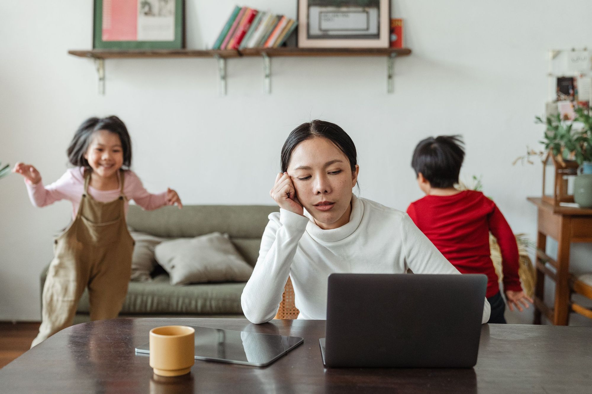 A mother working at a laptop while her children play around her