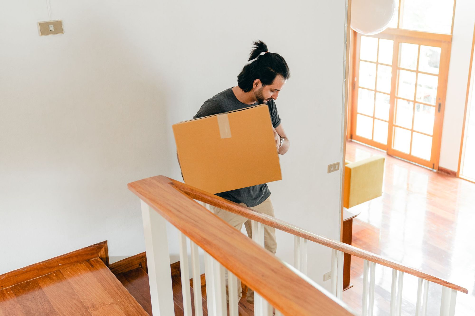 A man carrying a moving box through a bright home