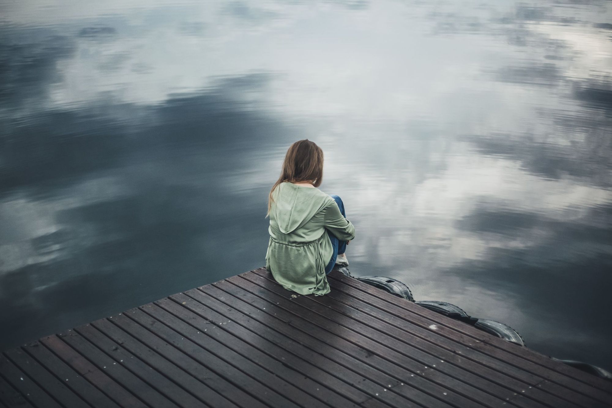 A person sitting at the end of a dock looking out over the water