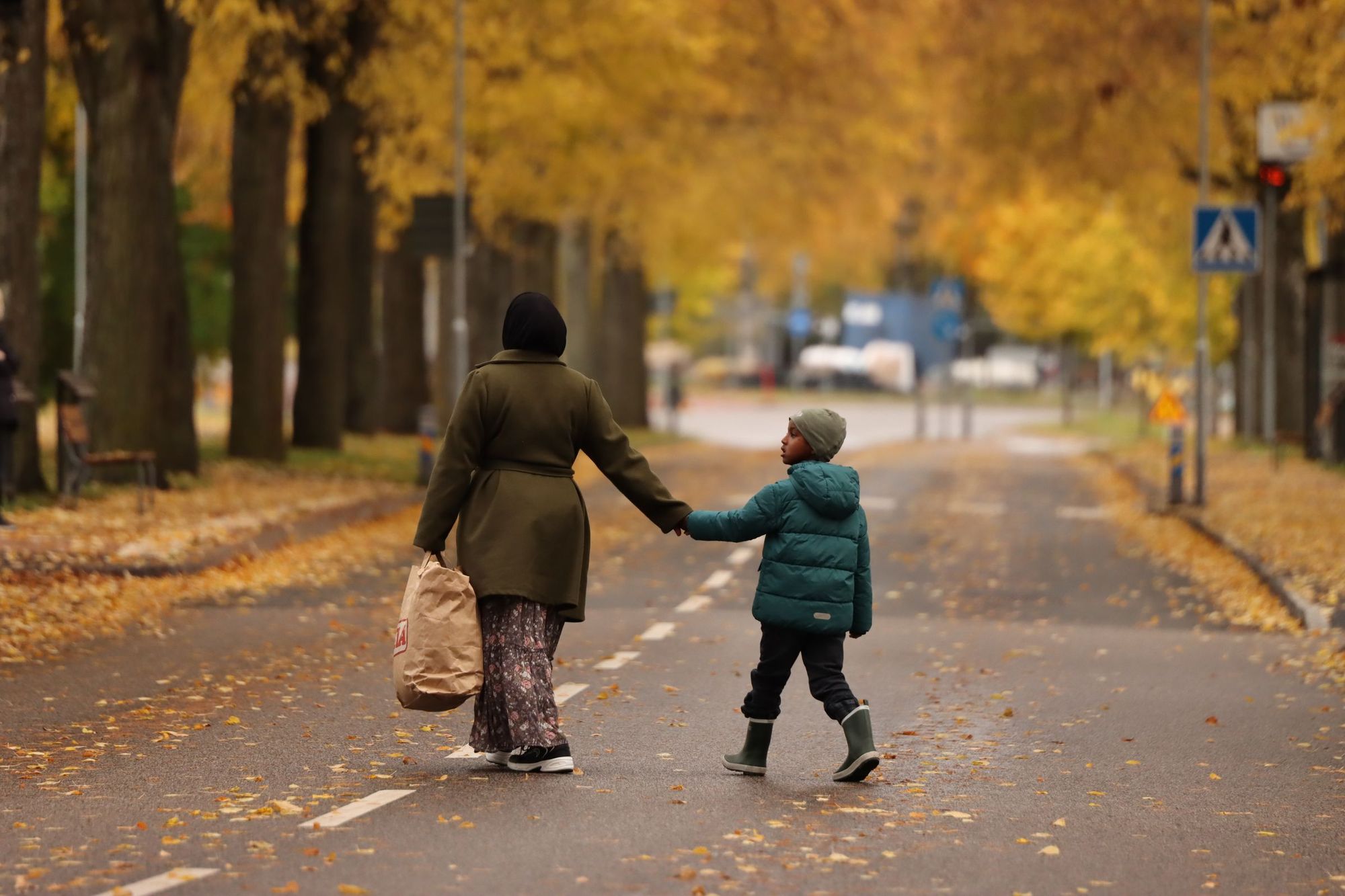 A mother and child walking hand in hand down an autumn street