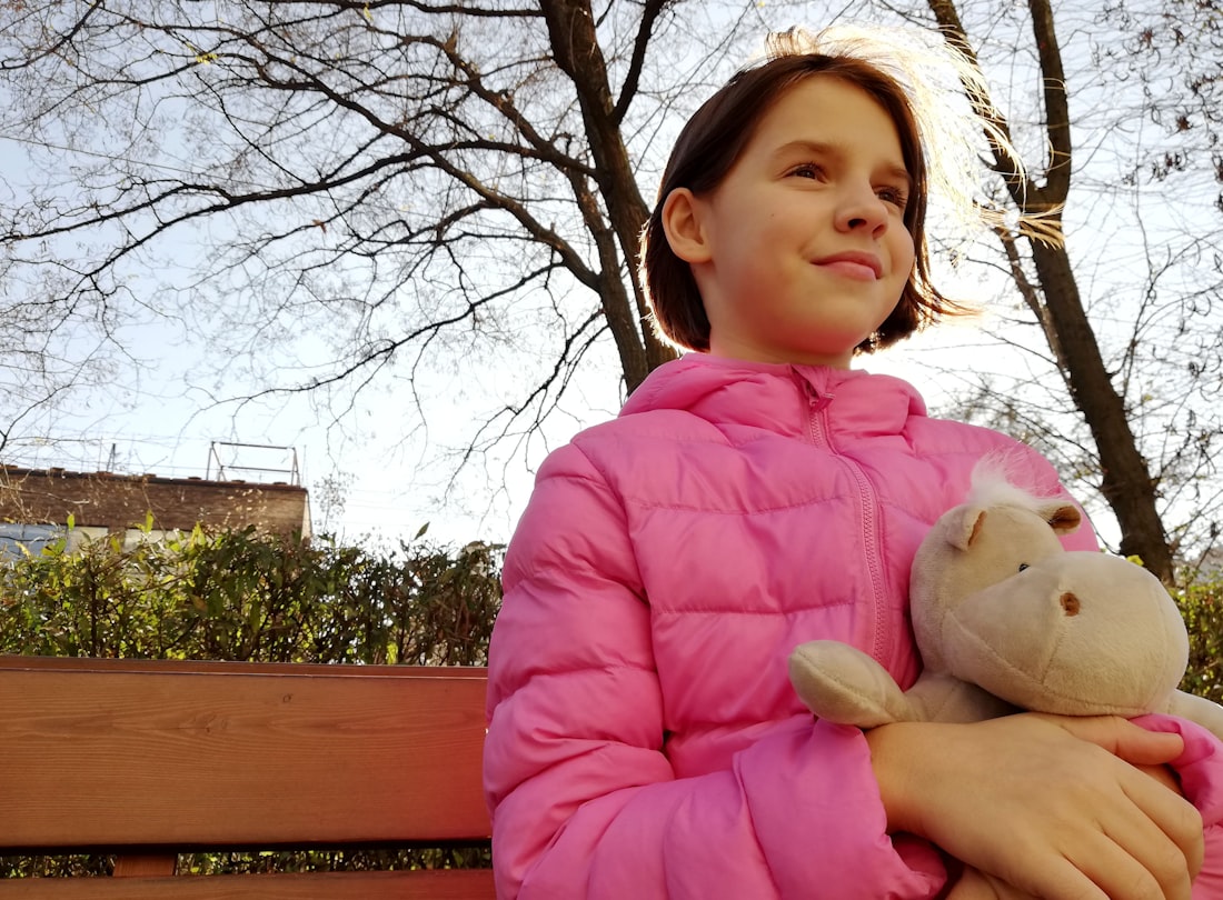 A child sitting outdoors holding a soft toy