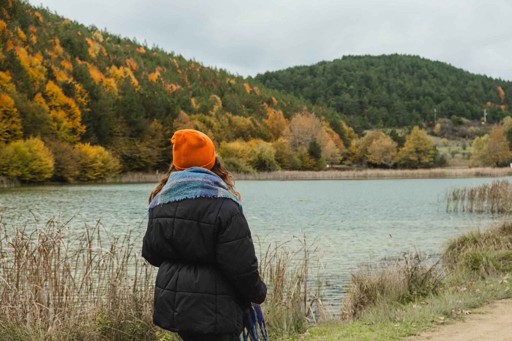 A person in an orange hat looking out over a lake and autumn hills