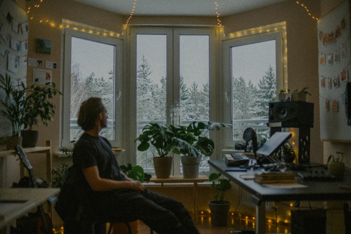 A man at a home desk with plants, looking out at snowy trees