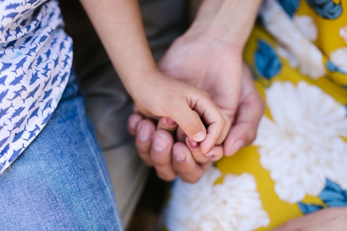 A small child's hand grips an adult's hand, resting on a yellow floral dress.