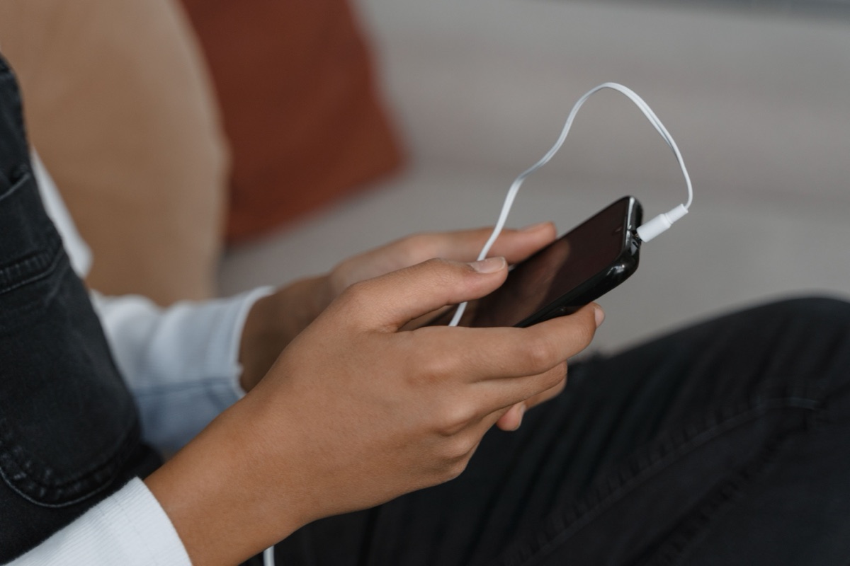 A young person's hands hold a smartphone with white earphones plugged in.