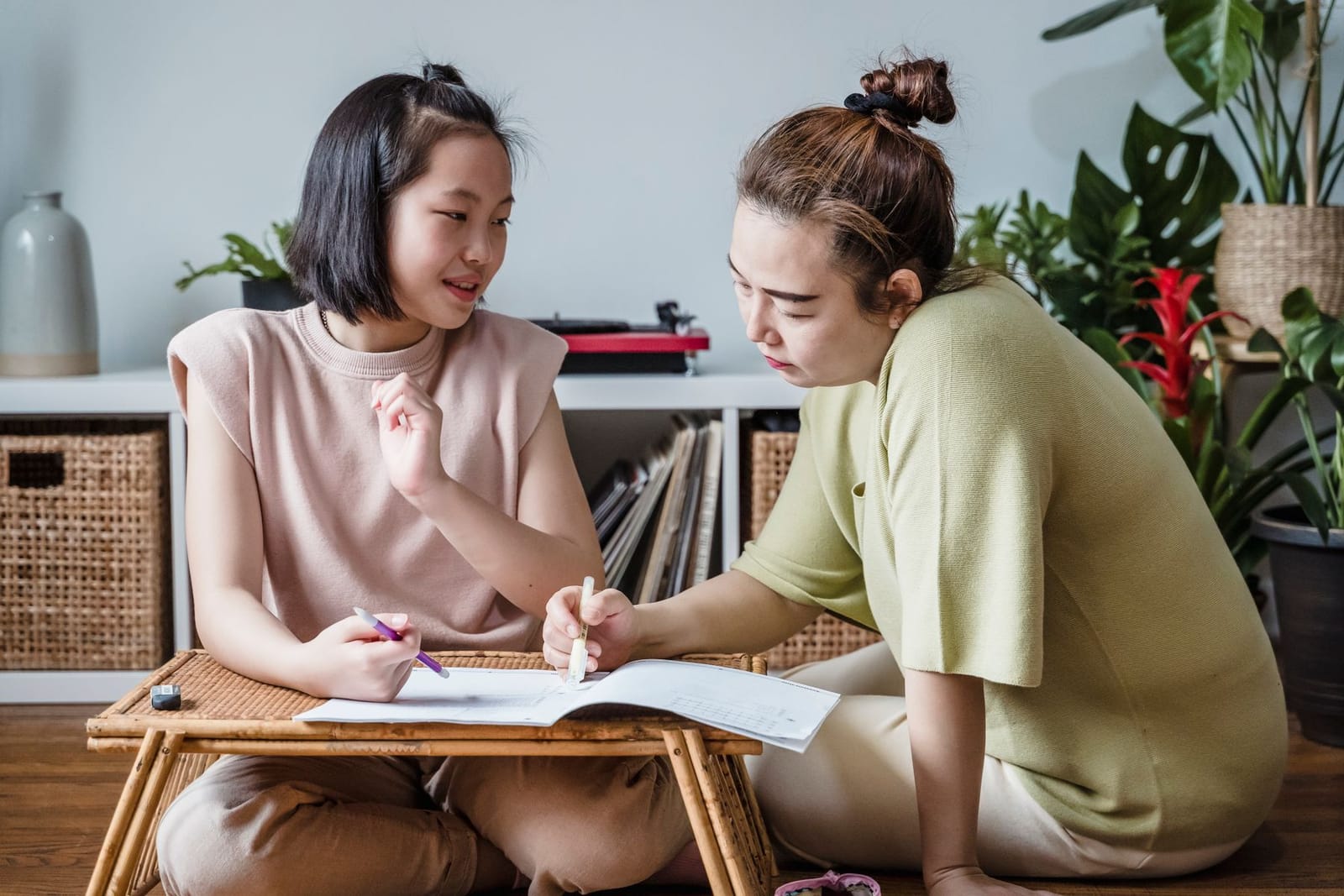 A woman and a girl working through a school booklet together at a low table at home