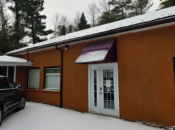 The outside of the Wasaga Beach office: an orange-brown building with a white door under a purple awning, and snow on the ground