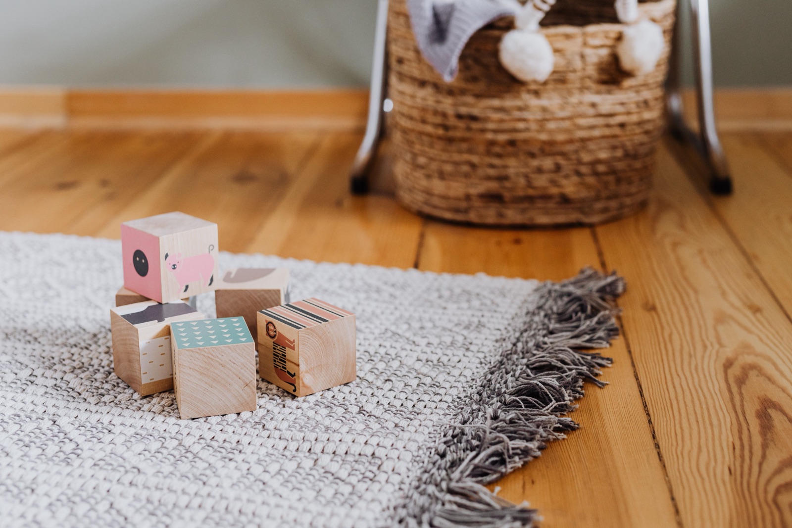 Painted wooden blocks are stacked on a woven rug beside a wicker basket.