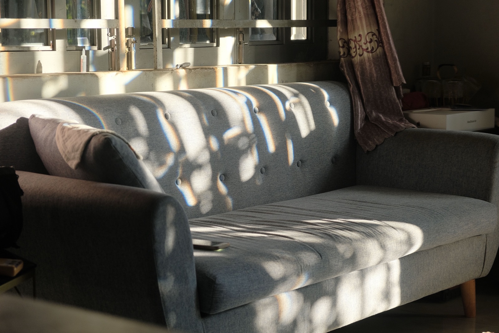 Dappled sunlight falls across a grey sofa in a living room.