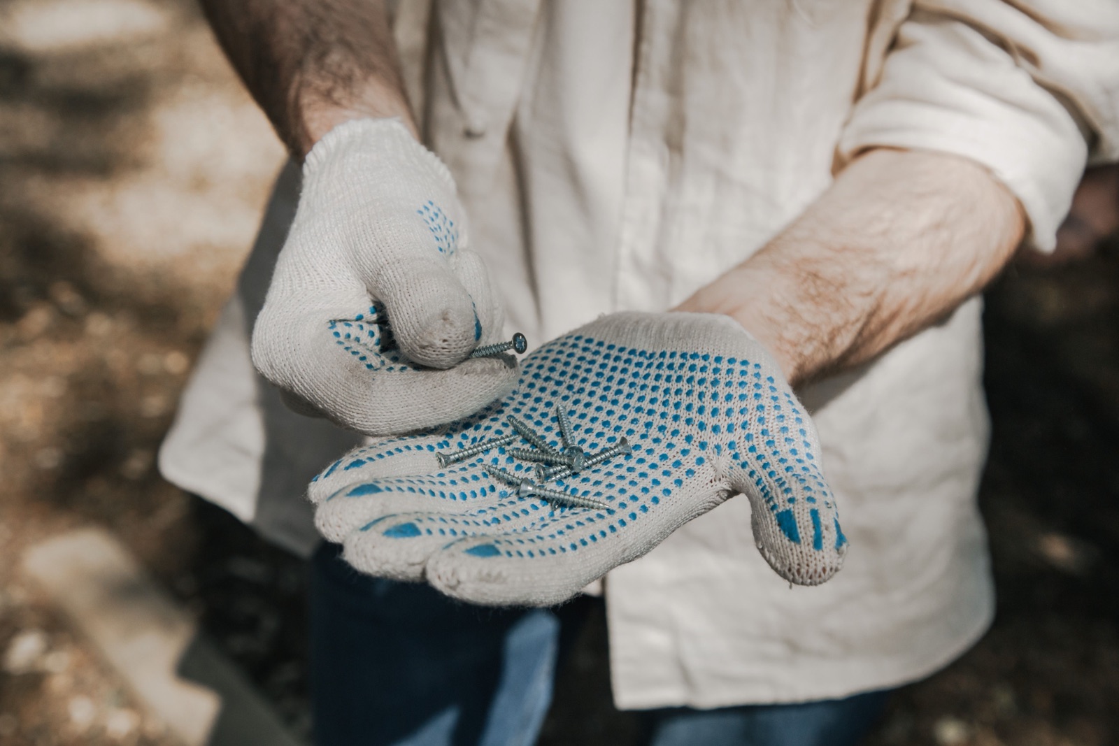A worker pulls on cotton work gloves, holding a few screws in one palm.