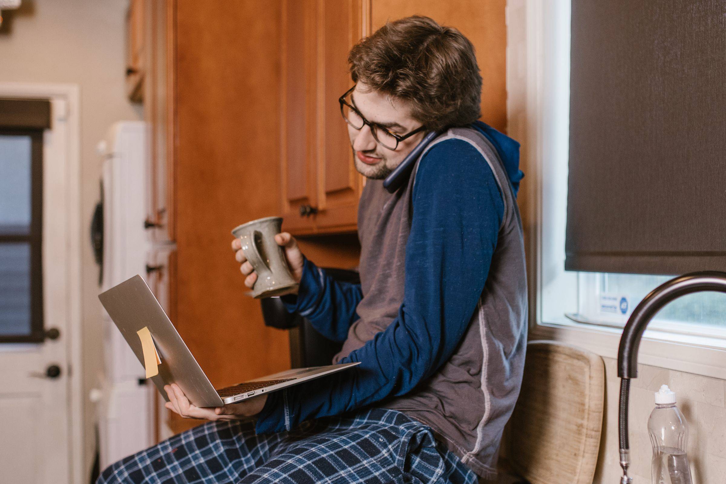 A man at home with a laptop and a mug, talking on the phone